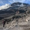 person in red jacket and black pants walking on rocky mountain during daytime