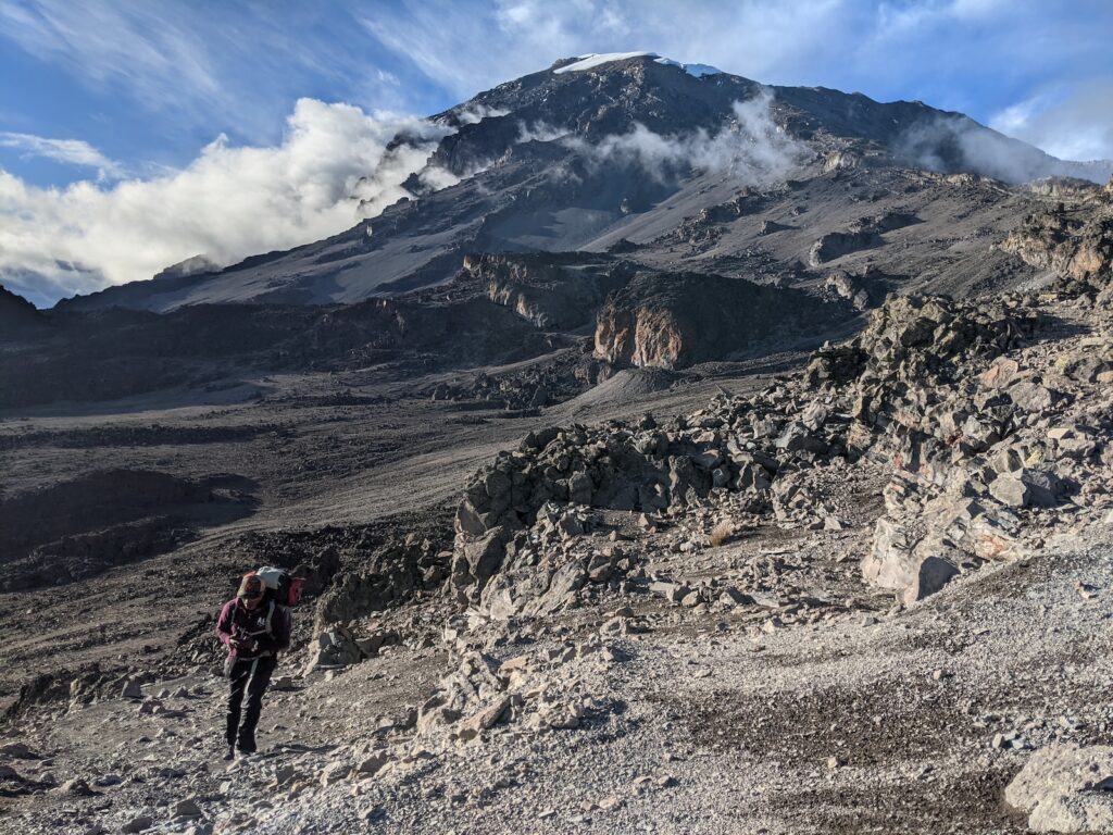 person in red jacket and black pants walking on rocky mountain during daytime